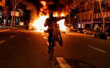 Un joven hace malabarismos con su bicicleta mientras un contenedor arde a su espalda el viernes por la noche en Barcelona. Nacho Doce / reuters/